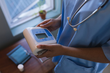 Female doctor holding blood pressure monitor at home