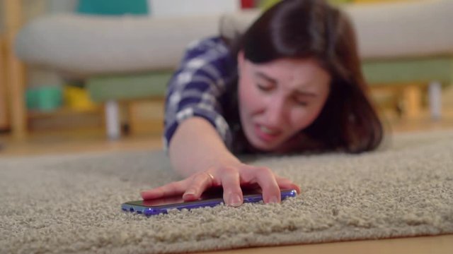 A young woman in a shirt had a heart attack and she tries to reach the smartphone lying on the floor slow mo