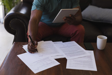 Senior man filling form while using digital tablet in living room