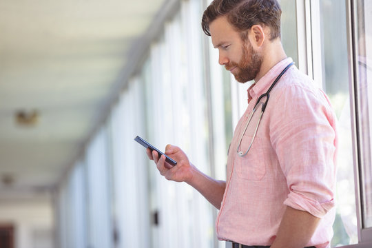 Male Doctor Using Mobile Phone While Standing At Nursing Home Corridor