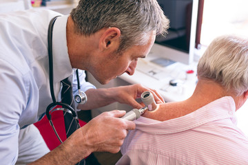 Male dermatologist examining senior patient with dermatoscopy