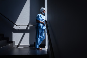 Female surgeon looking through the window in the hospital stairs