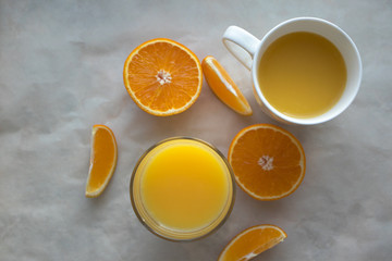 Top view of table with glass and cup of fresh orange juice and cut oranges on it
