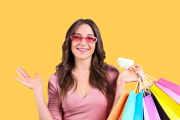 Black friday season sale concept. Attractive young woman with long brunette hair, wearing tight dress, holding many different blank shopping bags over yellow isolated background. Copy space, close up.