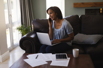 Woman talking on mobile phone while using laptop in living room