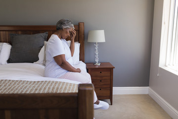Worried senior woman sitting on a bed at home