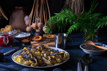 Sweet pasta dessert, noodles with poppy seeds, plum compote from fresh plums, dark background, blue table decorated with fresh flowers. Dry whole poppy plant in background.