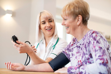 Female Nurse Measuring Blood Pressure Of Senior Woman At Home