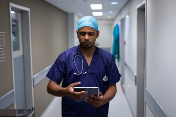 Male surgeon using digital tablet while standing at hospital corridor 