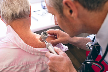 Male dermatologist examining senior patient through dermatoscopy