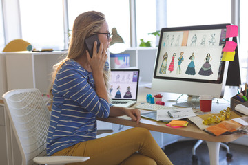 Female fashion designer talking on mobile phone while working at desk 