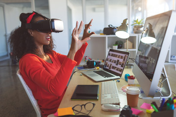 Female graphic designer using virtual reality headset at desk 