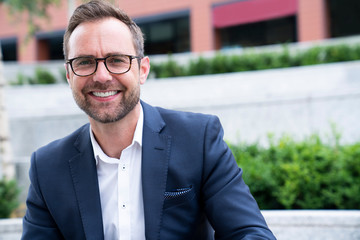 Portrait Of Smiling Mature Businessman Sitting At Outside Office Building