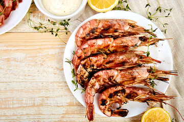 Grilled big tiger shrimps prawns on white plate with spices, lemon, fresh herbs on white wooden background, top view. Grilled seafood. Barbecue shrimps. Copy space.