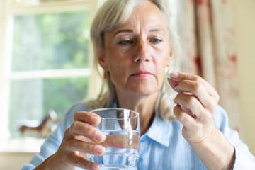 Senior Woman Taking Tablet With Glass Of Water At Home