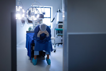 Upset female surgeon sitting on bed in operation room