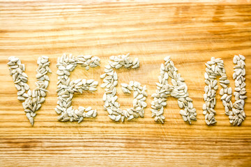 The word vegan is written with sunflower seeds on a wooden board. Healthy lifestyle