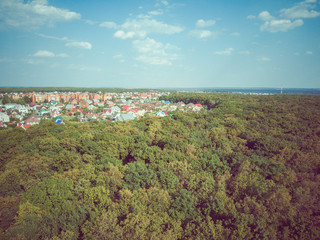 Aerial view of the green forest and village in the distance in summer.