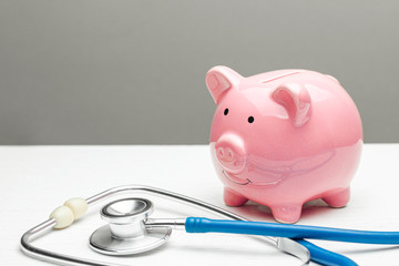 Pink piggy bank and stethoscope on a gray background. Concept of how to save on health insurance or personal insurance