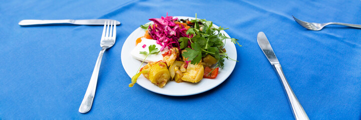 A plate full of food on a blue tablecloth. Dinner at the hotel, fried vegetables salad and cheese in a plate on a blue table.