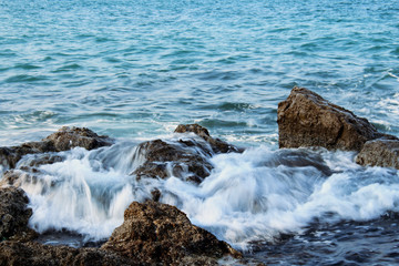 Foamy sea waves flowing on wet sea rocks on blue water background