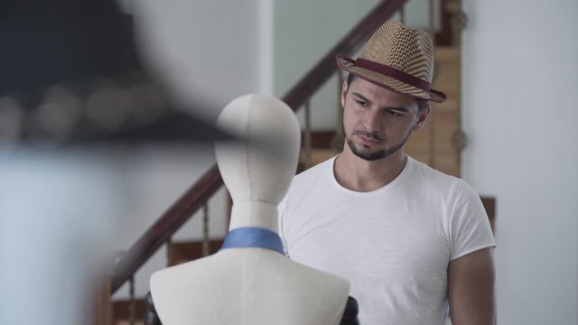 Portrait handsome young bearded handsome guy taking off his straw summer hat from a mannequin and putting on his head