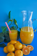 Homemade juice of satsuma mandarins and a group of satsuma mandarins on blue background with green leaves