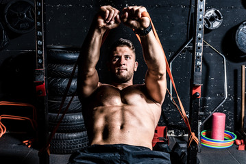 Young strong focused fit muscular man chest bench press stretching workout in improvised gym with rubber for strength and good looking of muscles dark image real people training