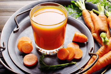 Vegetarian background of old fashioned tray with fresh organic carrots and juice on kitchen wooden table