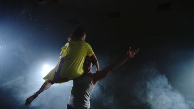 a couple twirling on the stage in spotlights and smoke
