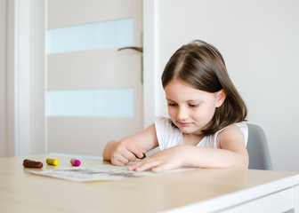 A 4-year-old girl draws with wax crayons against a white wall. drawing. Kid girl draws