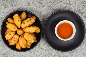 Fried rice balls called bolinho de arroz and pepper sauce in black plates in rustic background seen from above