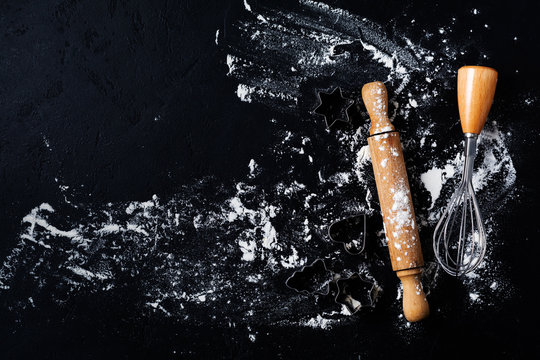 Rolling pin, cookie cutters and spatula with flour on dark black baking background, top view, copy space for text, menu, recipe. Flat lay.