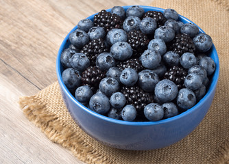 Bowl full of fresh blackberries and blueberries on a wooden background.