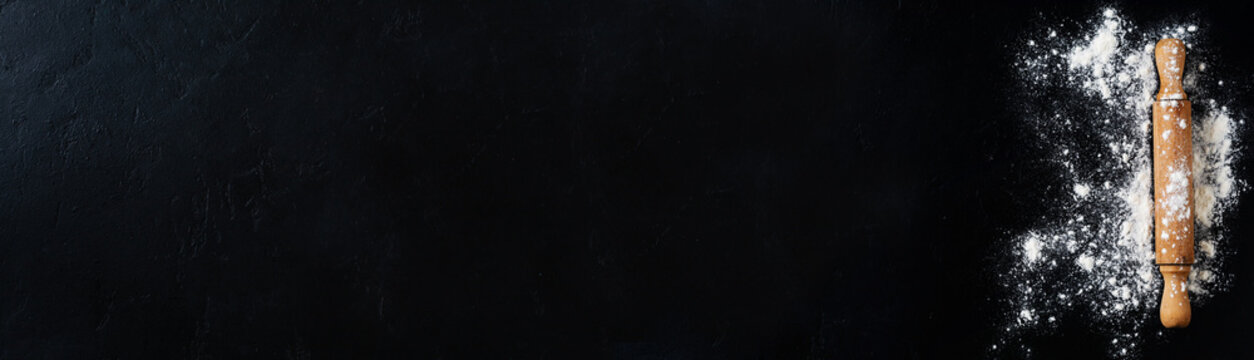 Rolling pin with flour on dark black baking background, top view, copy space for text, menu, recipe. Banner. Flat lay.