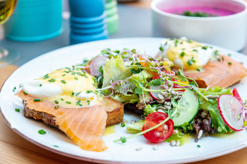 Two delicious poached eggs with salmon on toast served with mixed vegetables and lettuce in white ceramic plate