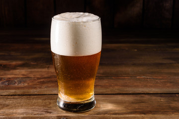 Glass of light beer on a dark pub. Glass beer on wood background with copy space. Full glass with lager beer, close up