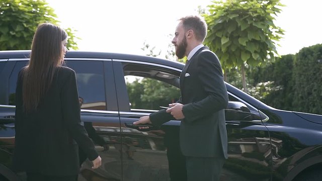 Gorgeous young couple approaching to the luxurious car ,man opening a door for woman and she sits in front seat