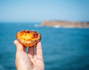 Fototapeta na wymiar pastel de nata in hand on a background of blue ocean, traditional portuguese food and desserts, travel to europe