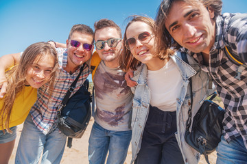 Company group of happy hugging young pretty people, students men and women on a sunny beach, vacation travel friendship day concept