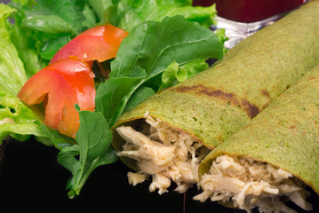 Spinach pancake stuffed with chicken breast and salad in black background close