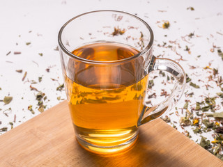 Glass mug with warm herbal tea on wooden board