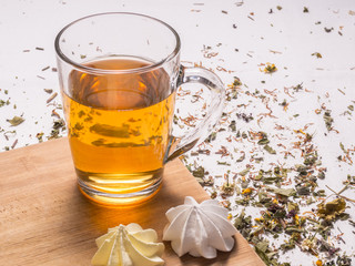 Composition with dried chamomile, glass mug with hot tea, meringues, bamboo board and dried herbal leaves and petals
