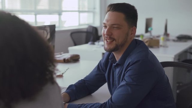 Professional young businessman sitting at table discussing work with female colleague smiling at workplace