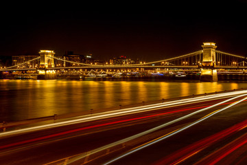 Fototapeta na wymiar The famous Chain Bridge in Budapest, Hungary, illuminated above the Danube river. Long exposure with light trails of cars at a night.