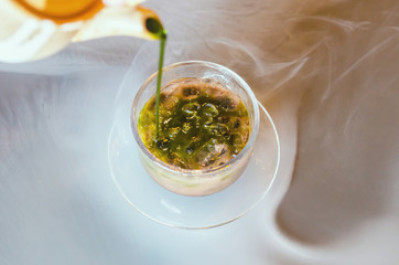 Hot green tea poured out of the teapot into the ice chocolate glass.