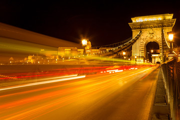 The famous Chain Bridge in Budapest with the Buda Castle at a background, Hungary. Long exposure with light trails of cars at a night.