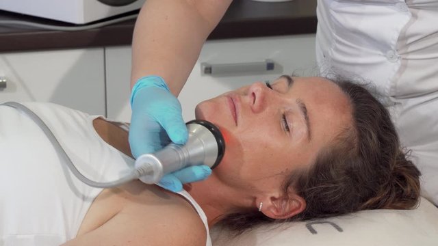 Mature lovely woman getting face rf-lifting treatment. Attractive woman receiving facial skin tightening procedure at beauty salon. Professional cosmetologist doing hardware skin treatment