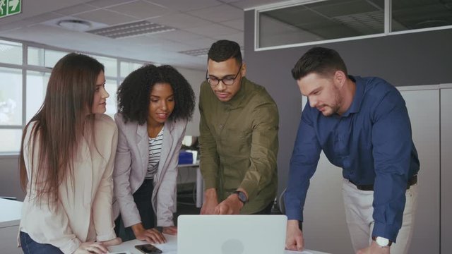 Happy young multi ethnic business team working together in teamwork on computer at office desk