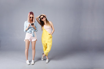 Social Internet Communication and Real Life. Cute stylish pink-head woman texting or surfing via social networks while her best friend outraged by lack of attention, poses over gray background